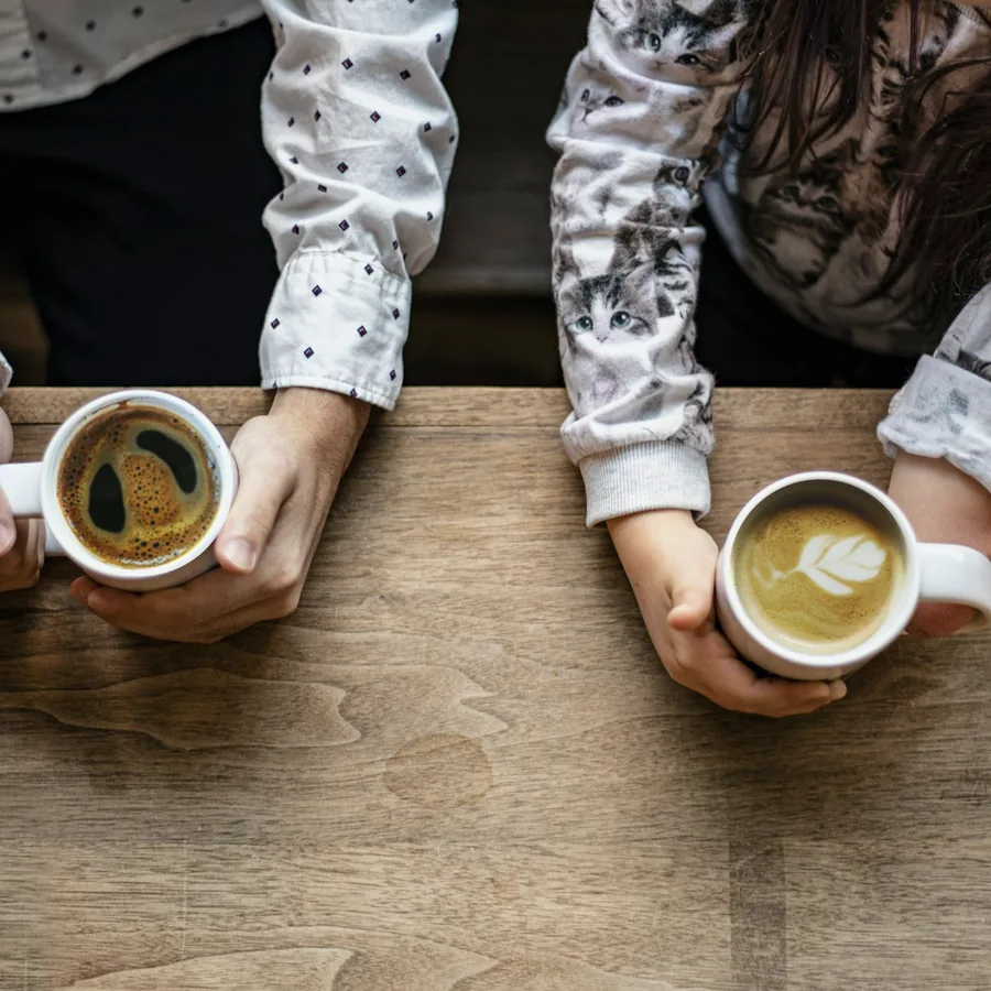 Deux paires de mains tenant chacune une tasse de café, posées sur une table en bois